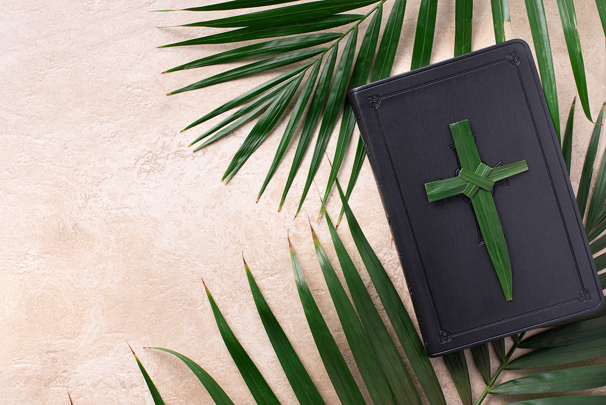 Palm Sunday concept. Palm cross on open Holy Bible and palm leaves. Reminder of Jesus sacrifice and Christ resurrection. Easter passover. Eucharist concept. Christianity symbol and faith